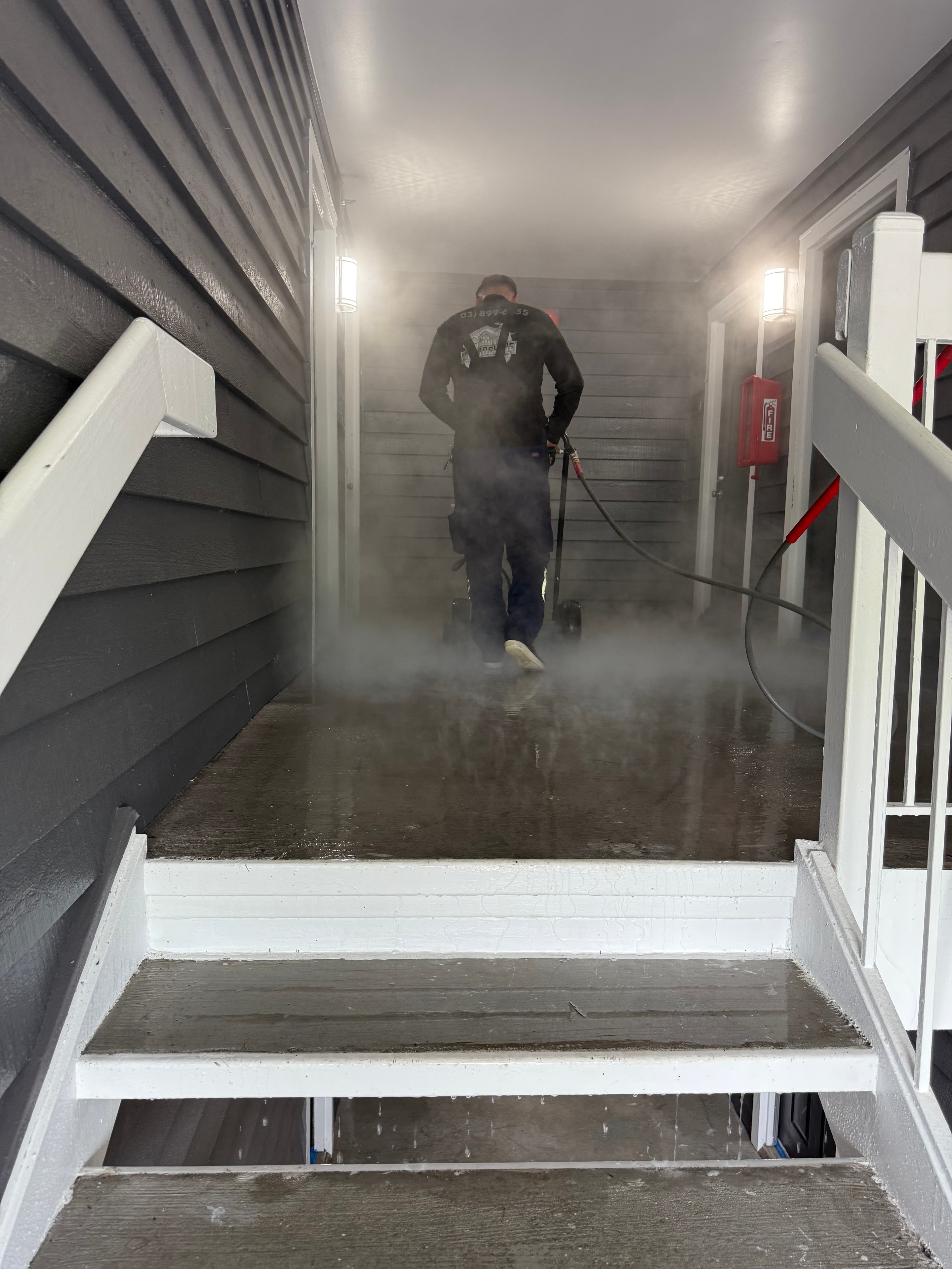 Worker pressure washing stairwell corridor